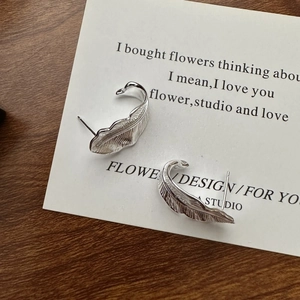 Elegant S925 sterling silver feather stud earrings with detailed texture on a card