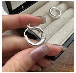 Dettaglio di orecchini a cerchio in argento sterling S925 con texture opaca e irregolare