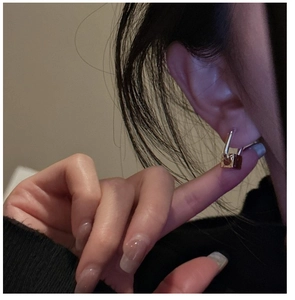 Close-up of dual-tone padlock earrings in silver and gold worn by a model in soft light