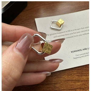 Detail of silver rectangular earring with gold hammered cube pendant in hand