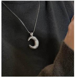 Detail view of a matte silver crescent moon pendant with hammered texture on a snake chain