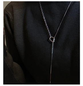 Detail of silver OT buckle long necklace with asymmetric snake and cross chain on sweater