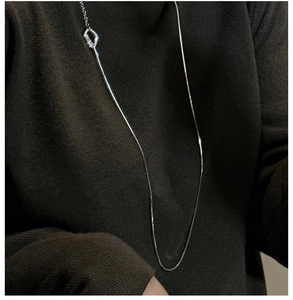 Detail of silver long necklace with OT buckle worn on a brown sweater close-up view