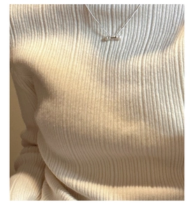 Detail of S925 silver necklace with pearl balance bar on white knit sweater
