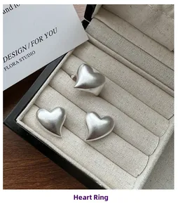 Macro shot of three matte silver heart rings in a linen jewelry box on a wood table