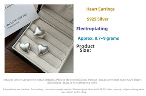 Macro detail of matte S925 sterling silver heart earrings on a soft beige jewelry display