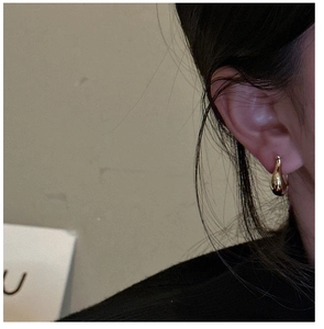 Gros plan de boucles d'oreilles gouttes dorées minimalistes en métal poli sur l'oreille