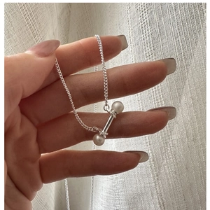 Detail showing hand holding an S925 silver necklace with white pearl barbell pendant