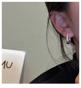 Gros plan d'une boucle d'oreille goutte en argent minimaliste portée avec des lignes fluides