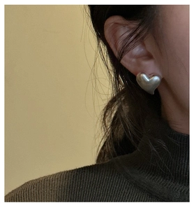 Close-up of matte silver heart stud earrings with brushed finish worn on the ear