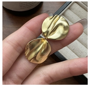Macro shot of matte gold irregular wrinkled disc earrings with textured metal finish