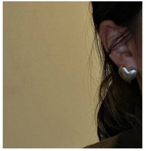 Close-up of minimalist matte silver heart stud earrings worn on model for modern style