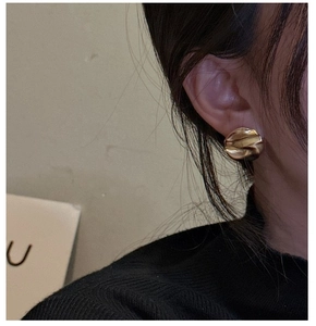 Macro detail of gold irregular wrinkled disk stud earring with textured surface on model