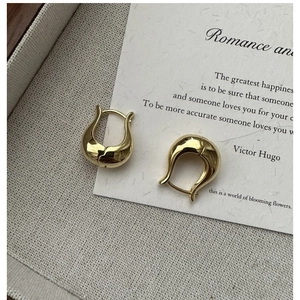 Détail des boucles d'oreilles en forme de U dorées sur fond de lin texturé avec citation
