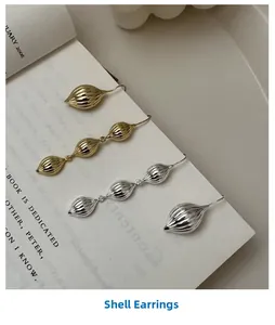 Détail de boucles d'oreilles coquillages dorées et argentées avec texture ondulée sur un livre
