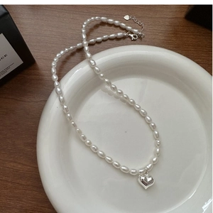 Détail macro du pendentif cœur en argent S925 et perles blanches sur céramique