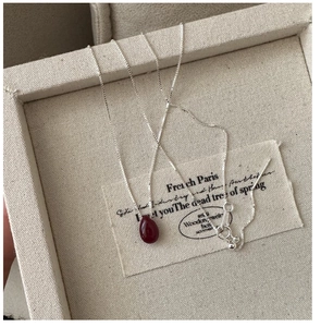 Detailed close-up of a silver S925 teardrop necklace with a red stone in a jewelry box