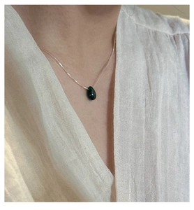 Close-up of elegant gold chain with a dark green water-drop gemstone on a white shirt