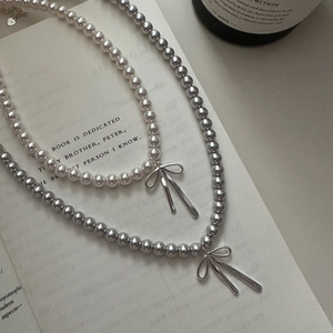 Detailed shot of S925 silver bow necklaces with white and grey pearls on a book