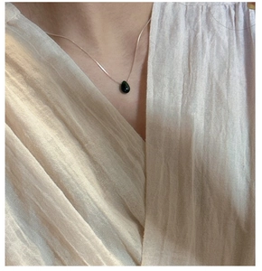 Close-up of a teardrop-shaped dark green stone pendant on a silver snake chain