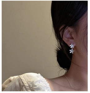 Primo piano di orecchini pendenti a fiore in argento indossati su uno sfondo beige