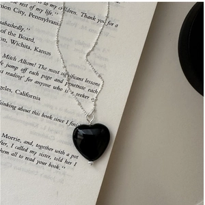 Macro shot of black onyx heart pendant on an elegant silver beaded chain over a book