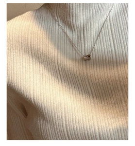 Close-up of a silver cylinder pendant necklace on a white ribbed turtleneck sweater