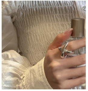 Detail of S925 silver crossover ring on hand holding a perfume bottle with soft lighting