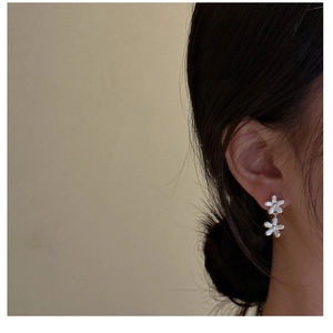 Dettaglio di orecchini a fiore in argento S925 indossati da una modella su sfondo beige