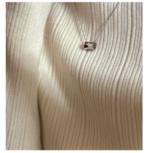 Close-up of a silver cylinder pendant on a delicate chain against a knit background