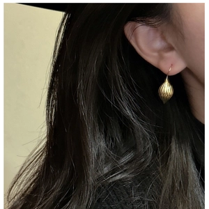Gros plan de boucles d'oreilles goutte dorées avec texture portée par un modèle