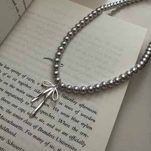 Detailed view of silver bow pendant and dark grey pearl necklace on a vintage book