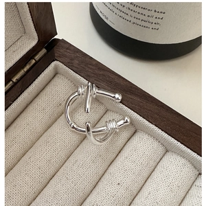 Close-up of a silver U-shaped intertwined ring on a beige velvet jewelry box cushion