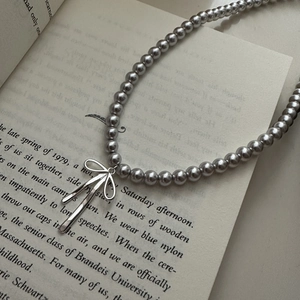 Elegant silver grey pearl necklace with minimalist bow pendant on an open book