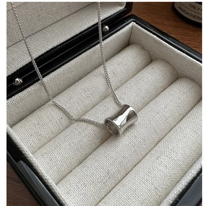 Macro shot of silver minimalist cylinder pendant on cross chain in black jewelry box