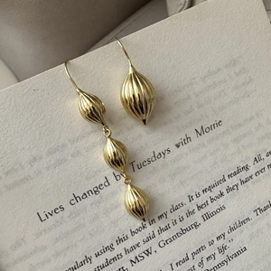 Boucles d'oreilles asymétriques en argent S925 avec perles dorées sur une page de livre