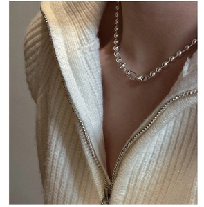 Detail of a minimalist silver ball chain necklace worn over a textured knit sweater