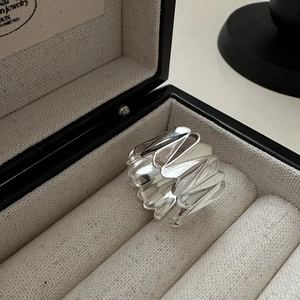 Gros plan d'une large bague argentée ondulée au fini poli sur un écrin de bijoux beige