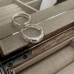 Détail de bagues argentées minimalistes superposées dans un écrin à bijoux rustique