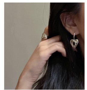 Close-up of minimalist heart earrings with black agate inlay and wide silver ring on model