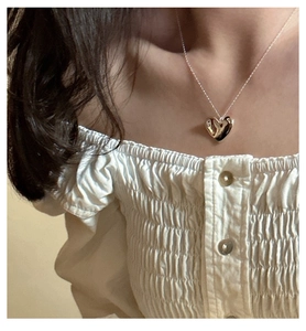 Close-up of a glossy gold heart pendant necklace worn on a woman's collarbone