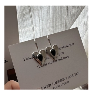 Close-up of heart-shaped silver earrings with black onyx drop on a minimalist display