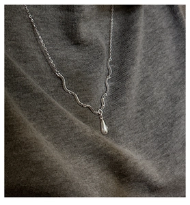 Détail du pendentif goutte d'eau argent S925 avec texture vague sur tricot gris
