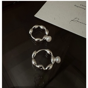 Macro detail of silver pearl earrings with organic twisted design on dark reflective surface