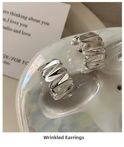 Détail de boucles d'oreilles argentées plissées en forme de C sur plateau blanc