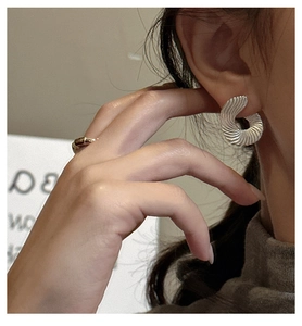 Macro shot of silver fan-shaped earrings with radial texture shown on ear