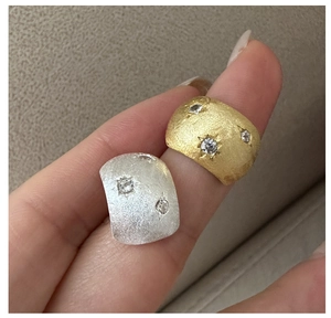 Detail of brushed silver and gold rings with three star-set zircons on wide textured bands