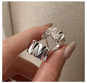 Détail de boucles d'oreilles géométriques argentées avec texture ondulée et design