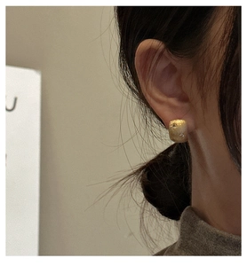 Detail of square gold earrings with brushed rock texture and shimmering small white stones