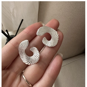 Detail of silver S925 fan-shaped earrings with spiral texture held in hand